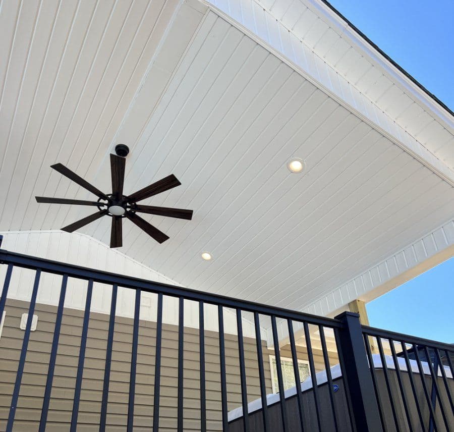Modern porch ceiling with a stylish ceiling fan and recessed lighting against a blue sky.